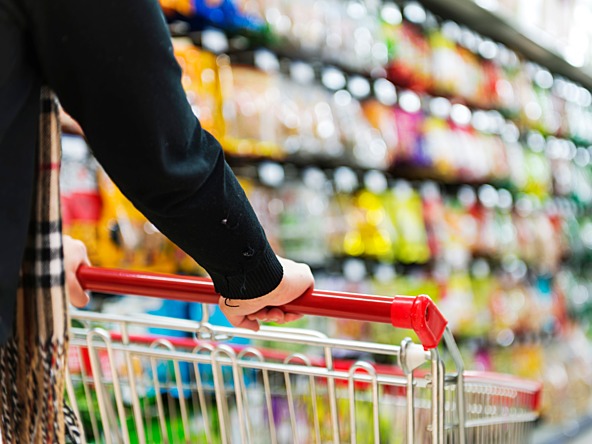 supermarket shopper pushing trolley in front of grocery shelves